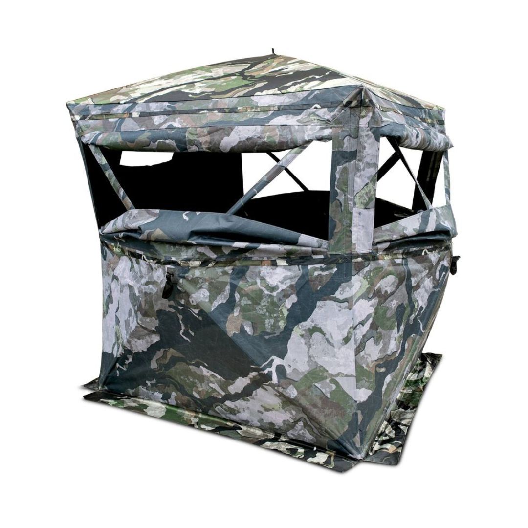 Un affût de chasse en tissu de camouflage, avec des ouvertures de fenêtres sur plusieurs côtés, monté sur un fond blanc.