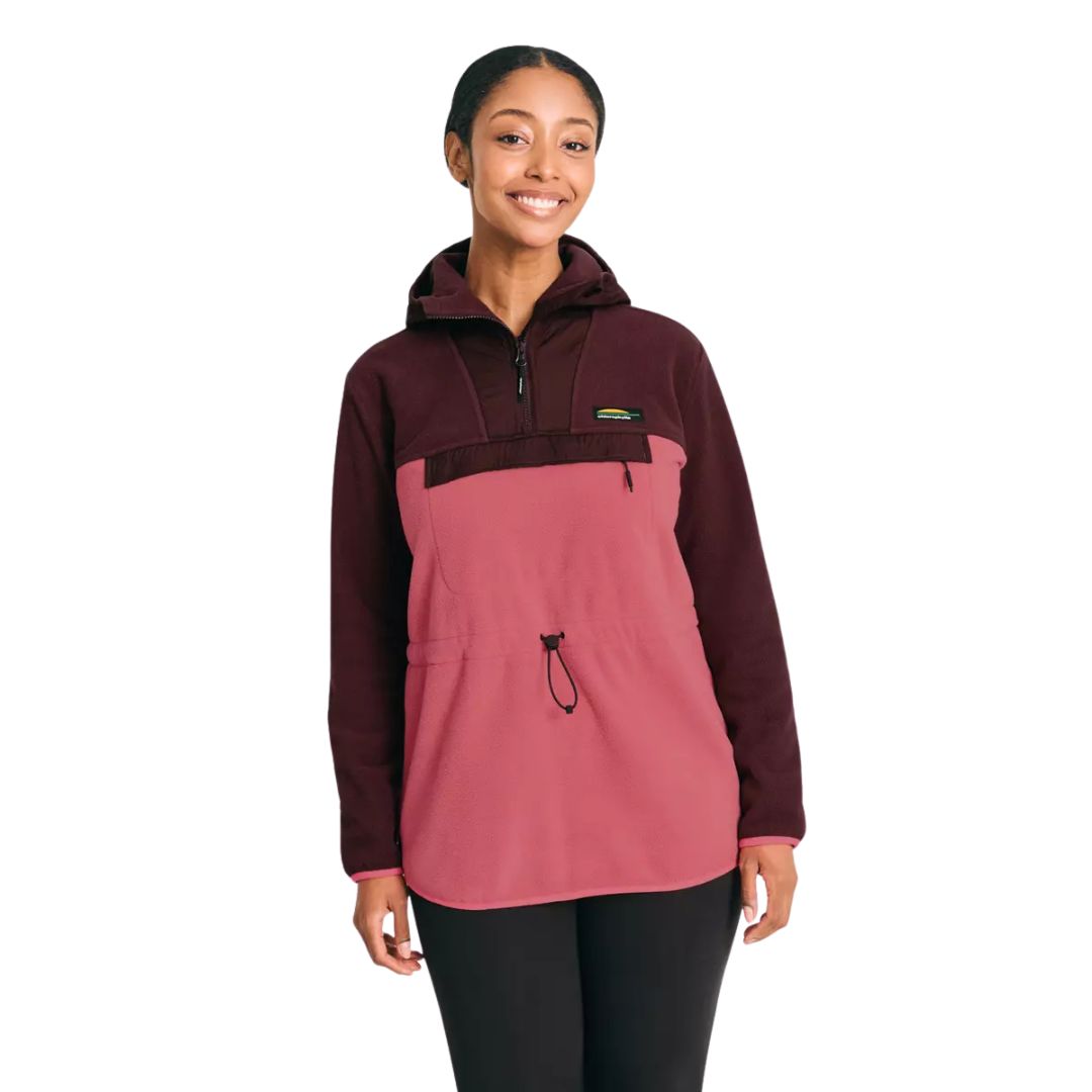 Une femme sourit en portant un pull-over en polaire bicolore marron et rose avec une capuche, une fermeture éclair sur le devant, une poche sur la poitrine et une taille ajustable. Elle se tient debout sur un fond blanc uni.