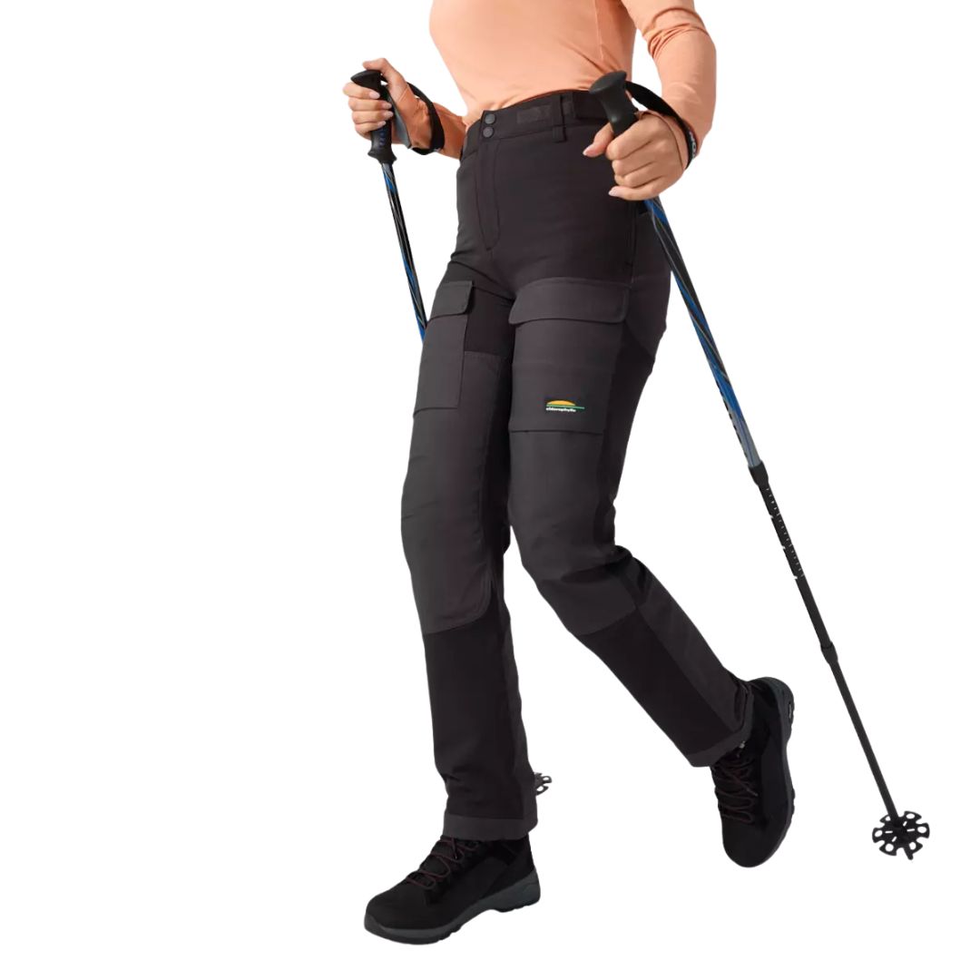 Une personne vêtue d'une chemise à manches longues de couleur pêche et d'un pantalon de randonnée noir marche avec deux bâtons de trekking. Seul le corps, à partir des épaules, est visible. La personne porte des bottes noires et se tient debout sur un fond blanc.