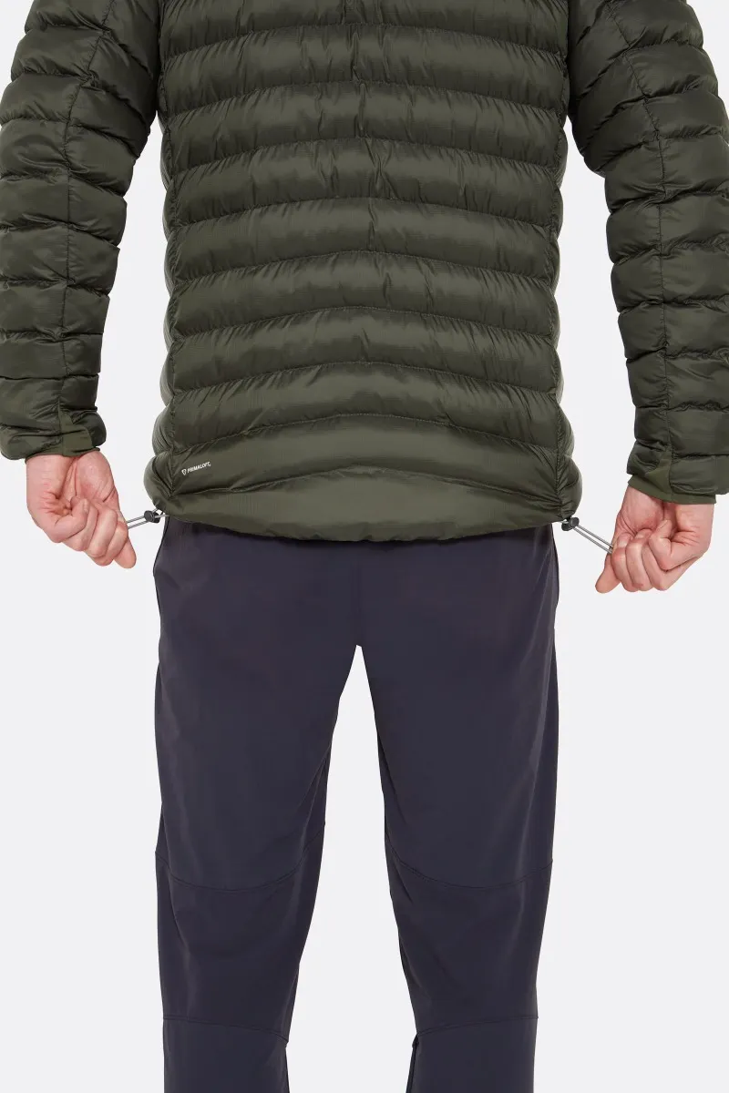 Une personne porte une doudoune vert foncé avec des cordons de serrage réglables à l'ourlet, associée à un pantalon foncé. L'accent est mis sur le design et les caractéristiques de la veste, mettant en valeur la texture matelassée et la fonctionnalité.