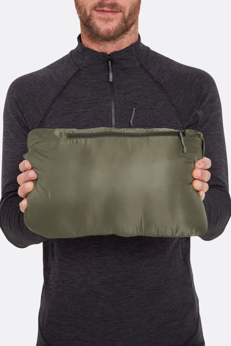 Une personne portant un haut à manches longues foncé tient une pochette compacte, vert olive, zippée, avec les deux mains sur un fond blanc uni.
