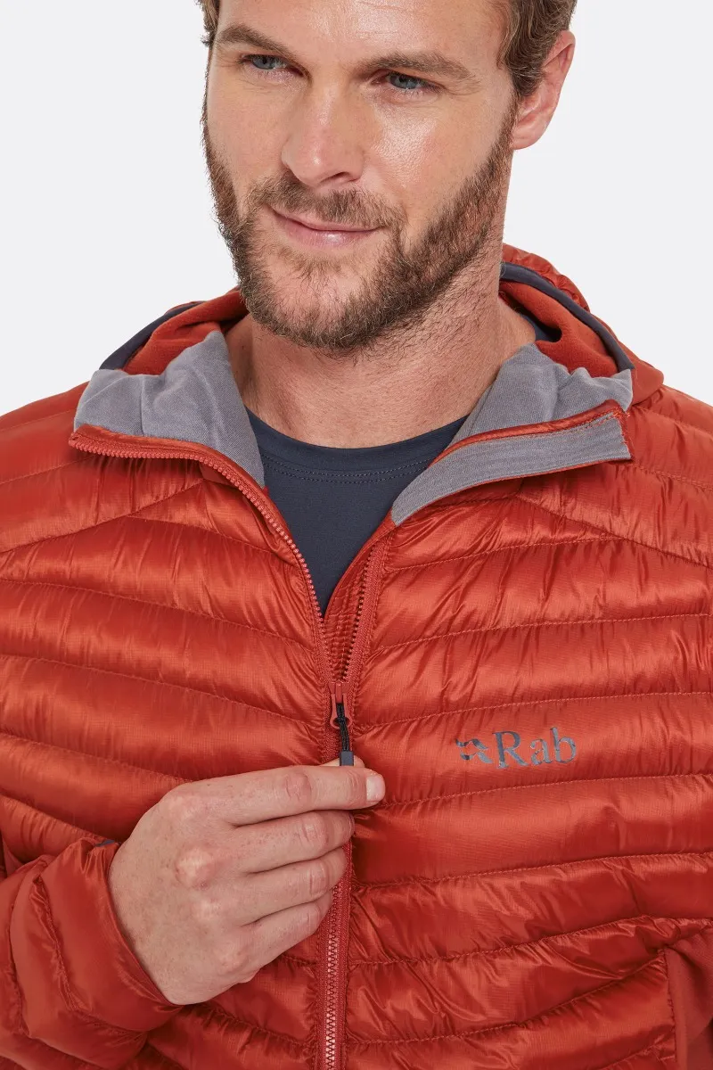 Un homme porte une doudoune rouge avec une capuche partiellement ouverte, révélant une chemise bleue en dessous. Il ajuste la fermeture éclair avec sa main droite. La veste porte la marque "Rab" sur la poitrine. Le fond est blanc uni.