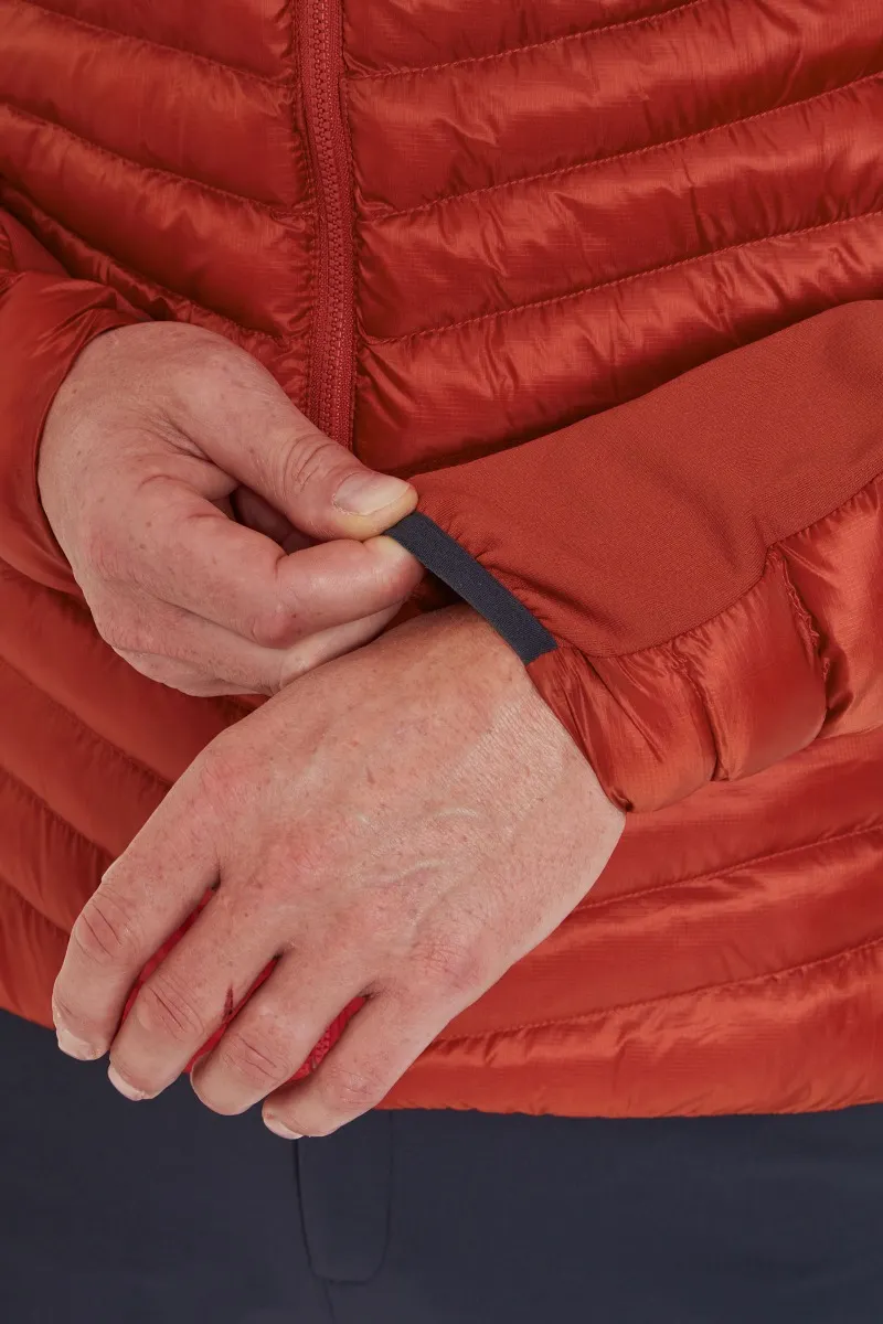 Une personne ajuste le revers d'une doudoune rouge. Ses mains sont légèrement patinées et elle porte un pantalon sombre. La veste présente des coutures matelassées horizontales et une fermeture éclair.