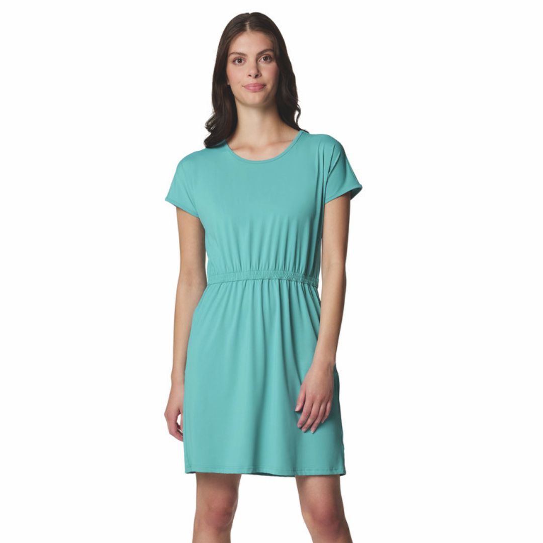 Une femme portant une robe turquoise à manches courtes, jusqu'aux genoux, avec une taille froncée, debout et regardant vers l'avant sur un fond blanc.