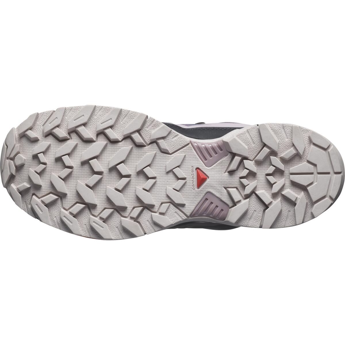 L'image montre la semelle texturée et robuste d'une chaussure de randonnée. Le motif de la bande de roulement est proéminent, avec des rainures profondes et un petit détail triangulaire rouge près du centre, conçu pour la traction et la stabilité sur un terrain accidenté.