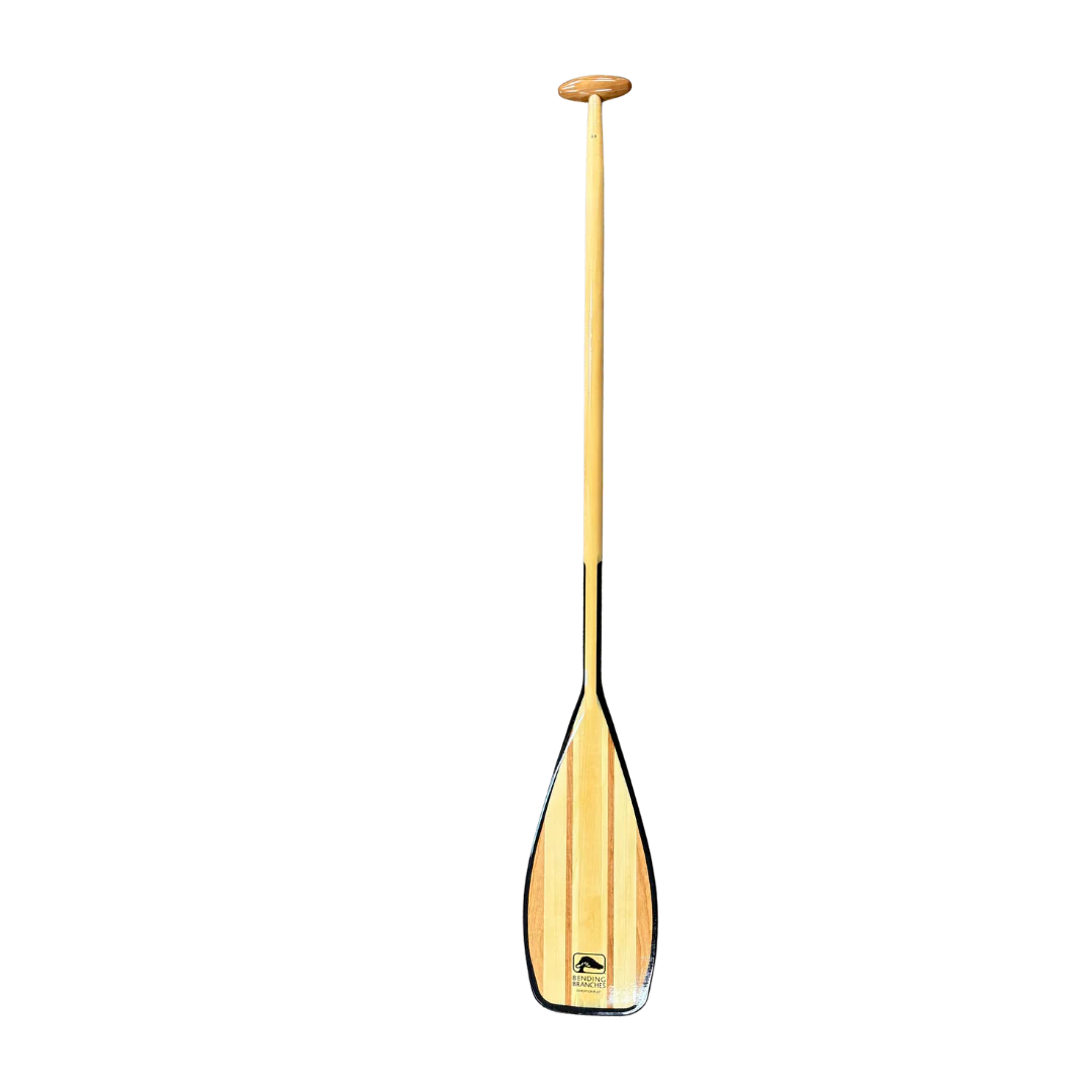 L'EXPEDITION PLUS est une pagaie de canoë en bois dotée d'un manche long et droit et d'une poignée ovale. Elle se caractérise par une pale large et plate, bordée de noir, et présente une finition en bois naturel. Photographiée sur fond blanc.