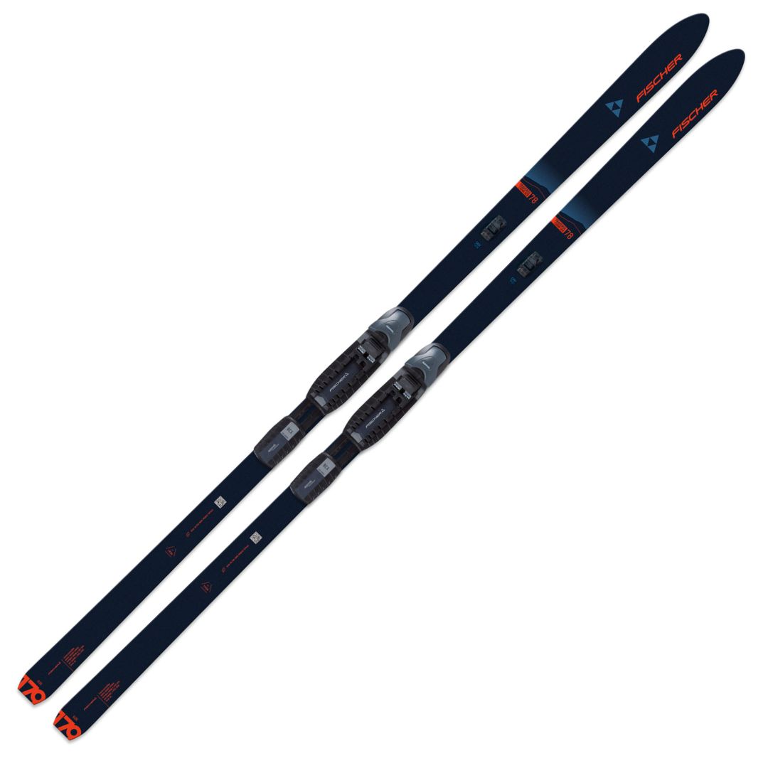 Une paire de skis de fond Fischer TRAVERSE 78 CROWN/SKIN XTRALITE bleu foncé avec fixations attachées, arborant des marques et des accents rouges et blancs sur les spatules et les côtés, positionnés parallèlement sur un fond blanc.