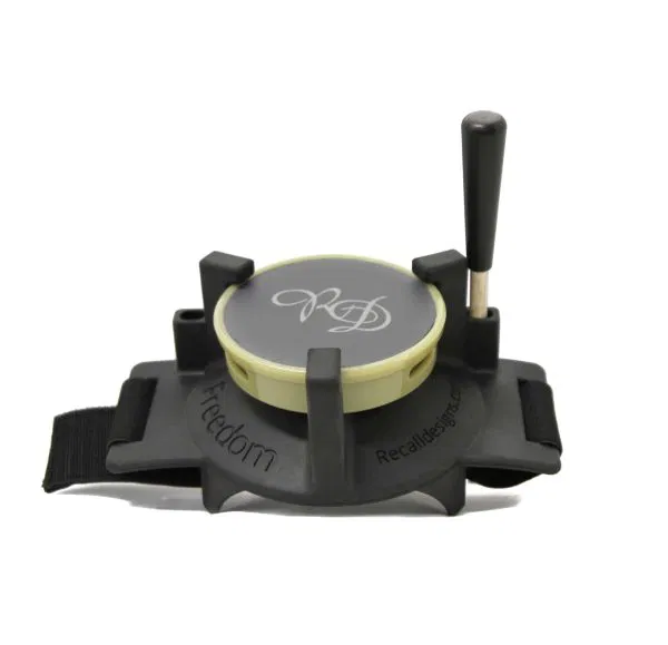 Appareil rond de dressage de chiens à main, avec une base noire, une partie supérieure jaune clair, un levier sur un côté et des sangles pour l'attacher. La partie supérieure porte un monogramme décoratif et le mot "Freedom" est visible sur la base.