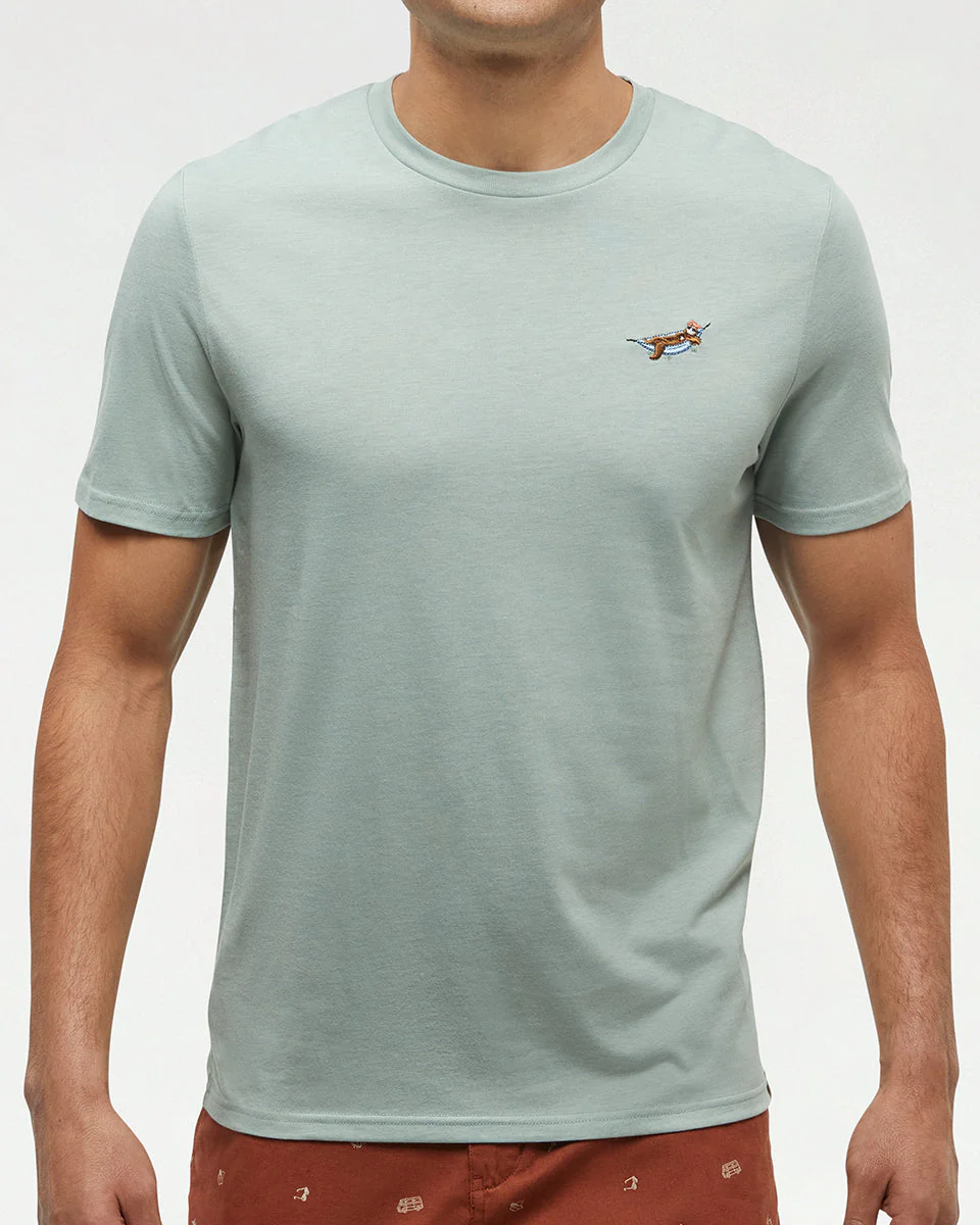 Une personne porte un t-shirt vert clair à manches courtes orné d'un petit chien brodé sur la poitrine gauche, ainsi qu'un short brun-rouge. Son visage n'est pas visible.
