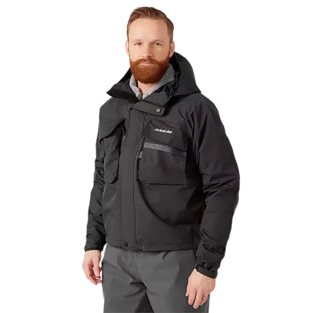 Un homme barbu se tient debout, légèrement tourné vers le côté, regardant la caméra sur un fond blanc, portant le MANTEAU DE WADING GUIDELINE KAITUM (3XL) et un pantalon gris.