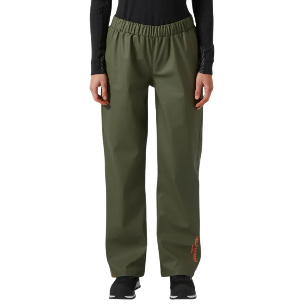 Une personne porte le pantalon W GALE RAIN PANT de couleur vert olive, caractérisé par une coupe ample, une ceinture élastique et une inscription orange discrète sur le bas de la jambe gauche, associé à un haut noir à manches longues. Elle se tient debout, face à l'objectif.