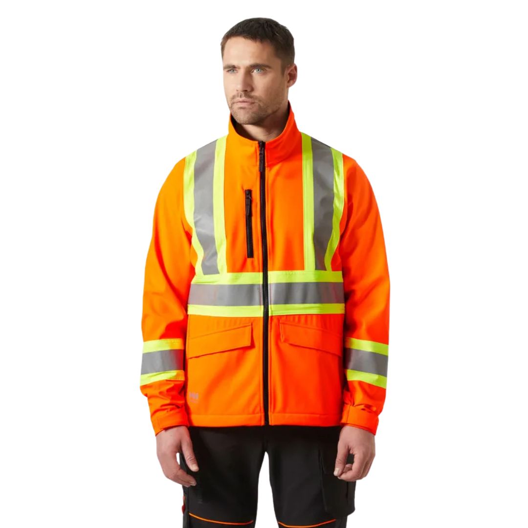 Un homme se tient debout, le regard tourné vers l'avant, l'air impassible. Il porte la VESTE SOFTSHELL HAUTE VISIBILITÉ HELLY HANSEN ALTA 2.0 SOFTS CSA POUR HOMME, une veste softshell orange haute visibilité ornée de bandes réfléchissantes argentées.