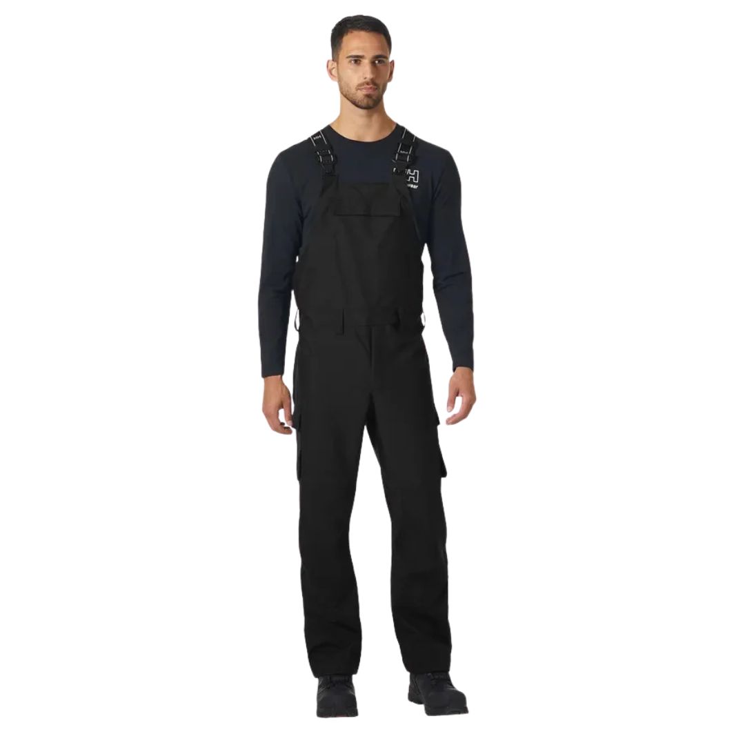 Un homme portant une SALOPETTE DE TRAVAIL HELLY HANSEN WORKWEAR OXFORD POUR HOMME noire par-dessus une chemise à manches longues.