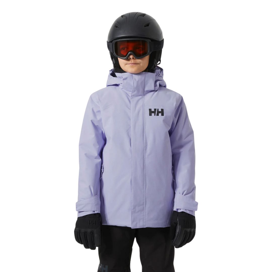 Un enfant portant une veste Helly Hansen violet clair, un casque de ski noir, des lunettes teintées de rouge, des gants noirs et un pantalon noir, debout sur un fond blanc uni.