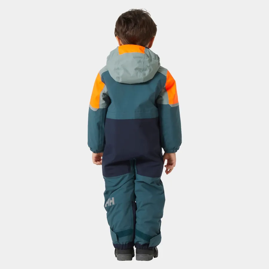 Un enfant porte une combinaison de neige colorée à capuche et se tient dos à la caméra. La combinaison présente des nuances de bleu, d'orange et de vert. L'enfant porte également des bottes d'hiver grises et se tient debout sur un fond blanc uni.