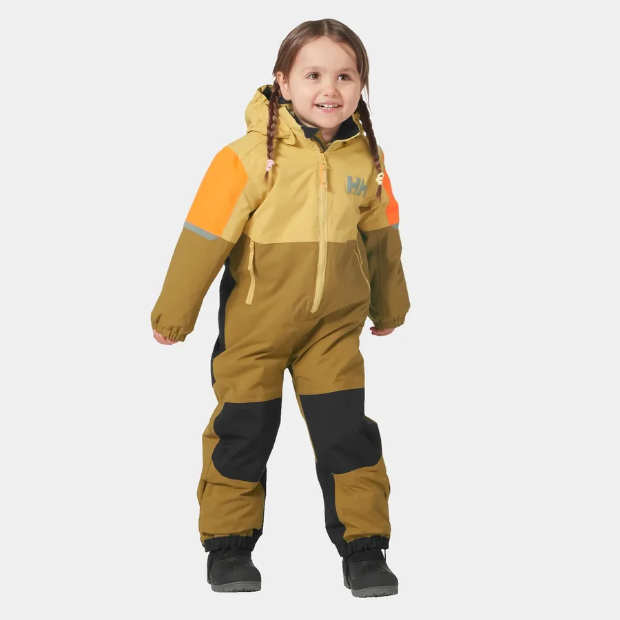 Un jeune enfant avec des nattes sourit et porte une combinaison de neige d'hiver aux couleurs contrastées dans des tons de jaune, d'orange et de noir. La combinaison de neige a une capuche et des bandes réfléchissantes sur les manches. L'enfant se tient debout devant un fond blanc uni.