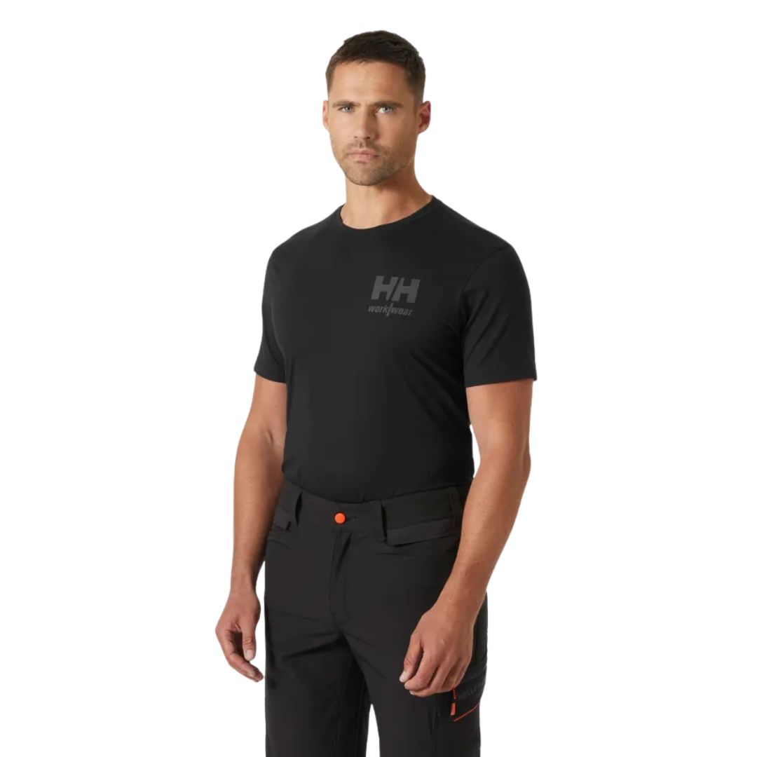 Un homme portant un t-shirt noir « CLASSIC LOGO 2.0 » avec un logo gris sur la poitrine et un pantalon de travail noir.