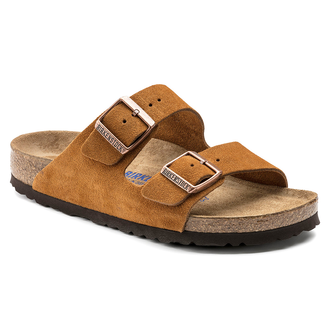 Une paire de sandales Birkenstock Arizona unisexe. Les sandales sont composées de deux larges bandes en daim souple de couleur marron clair. Elles ont deux boucles métalliques réglables pour un ajustement optimal. Les semelles sont en caoutchouc noir et présentent un motif rainuré pour une meilleure adhérence.