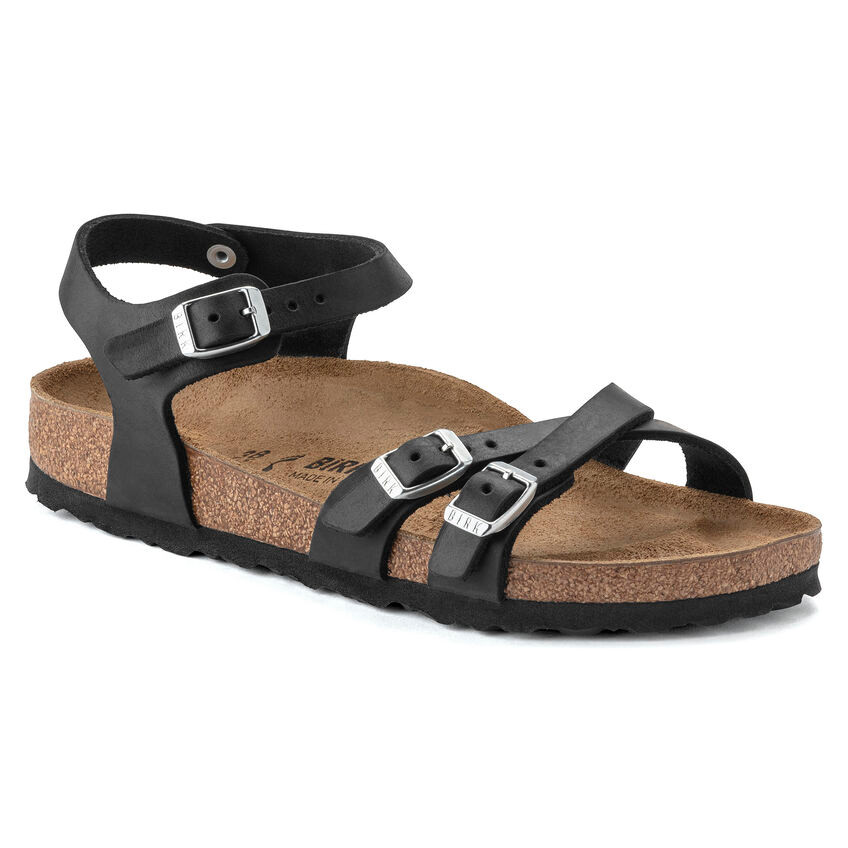 La SANDALE BIRKENSTOCK KUMBA EN CUIR HUILÉ POUR FEMME présente des brides noires avec trois boucles argentées, une assise plantaire en liège, une semelle en caoutchouc noir, une bride de cheville et deux brides de pied.