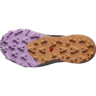 L'image montre la semelle d'une chaussure avec un motif de bande de roulement robuste. Le côté gauche est violet et le côté droit est beige, avec un petit triangle rouge au milieu. Le design semble avoir des crampons profonds et multidirectionnels pour la traction.