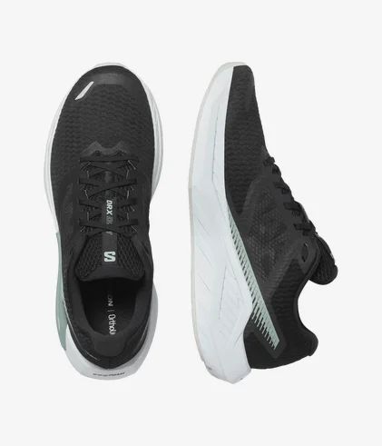 Une paire de chaussures de course noires et blanches avec une tige en mesh texturé et une semelle blanche épaisse. Les chaussures ont des lacets et un logo discret sur le côté et la languette. Une chaussure est présentée de dessus et l'autre de côté.