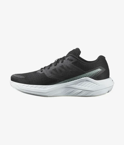 Une chaussure de course athlétique noire avec une tige en mesh texturé et une semelle épaisse et coussinée blanche. La chaussure présente un logo discret sur le côté et un design élégant et moderne adapté aux tenues de sport ou décontractées.