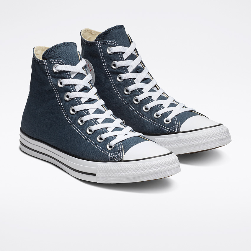 Une paire de baskets montantes bleu marine foncé avec lacets blancs et bout en caoutchouc. Elles présentent un design classique avec une bande noire sur la semelle en caoutchouc blanche, positionnée sur un fond blanc uni.