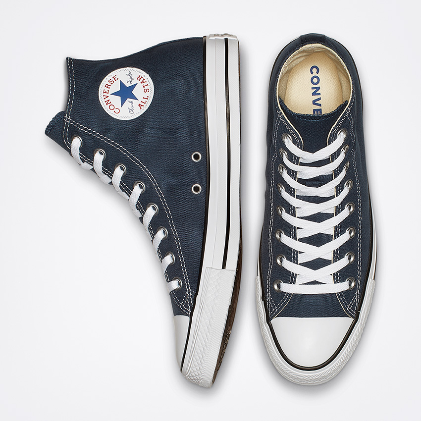 Une paire de baskets Converse montantes noires. Une chaussure est positionnée de côté, laissant apparaître le logo circulaire emblématique, tandis que l'autre est verticale, laissant apparaître le devant et les lacets. Le tout sur fond blanc.
