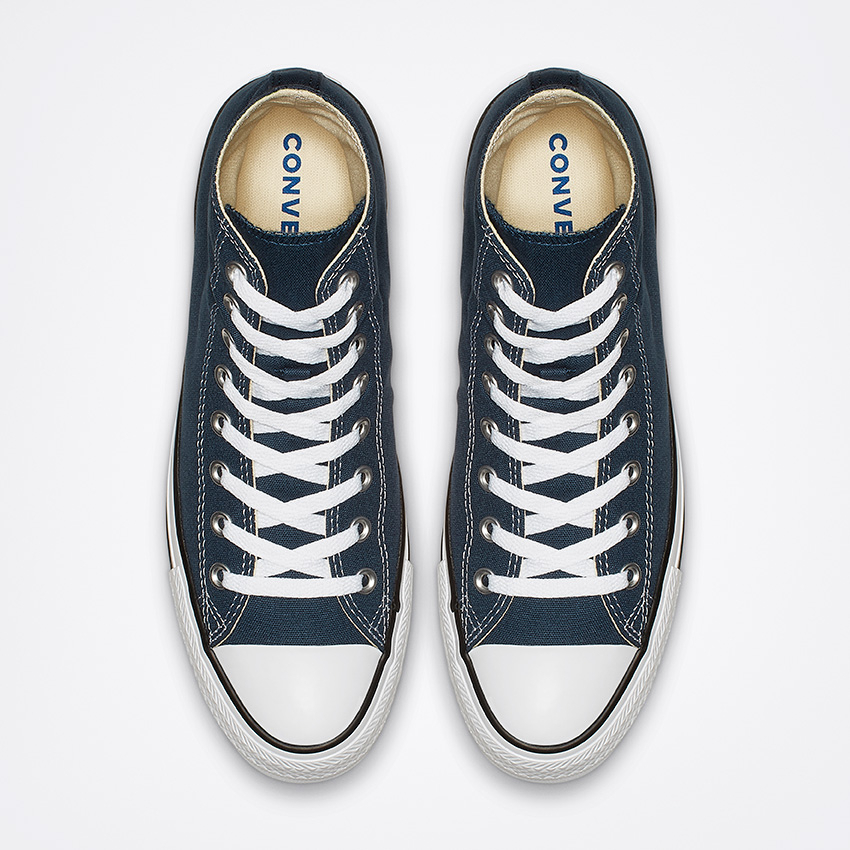 Vue de dessus d'une paire de baskets montantes bleu foncé à lacets blancs et semelles en caoutchouc. Le mot « CONVERSE » est visible à l'intérieur du talon des deux chaussures. Elles sont placées côte à côte sur un fond blanc.