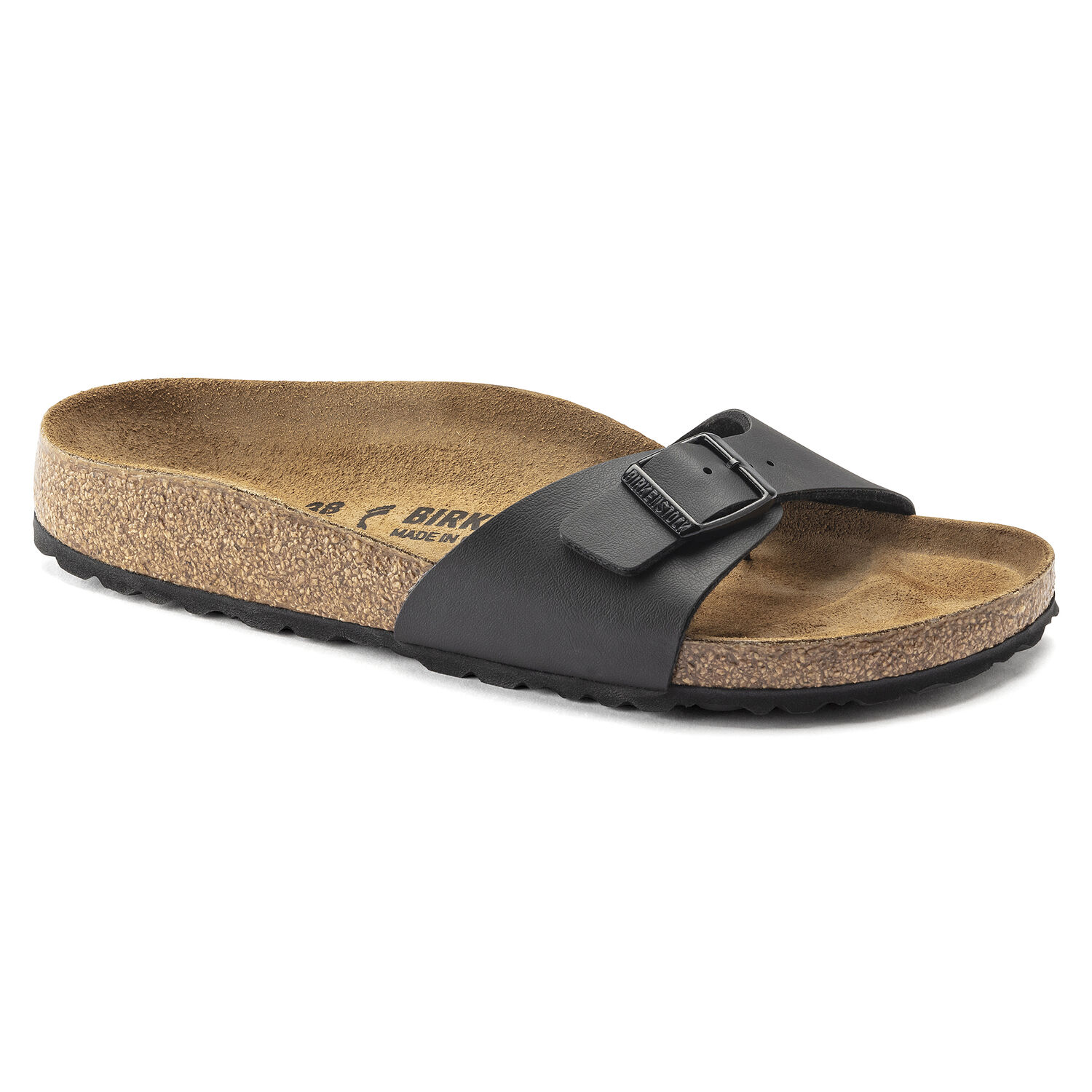 Une paire de sandales Birkenstock Madrid Birko-Flor étroites en noir sur un fond blanc. Les sandales ont une seule bride réglable avec une boucle en métal. La bride est en Birko-Flor, un matériau synthétique ressemblant au cuir qui est doux, durable et facile à nettoyer. Le lit de pied est en liège anatomique et possède une doublure en suède. La semelle extérieure est en EVA, un matériau léger et absorbant les chocs.