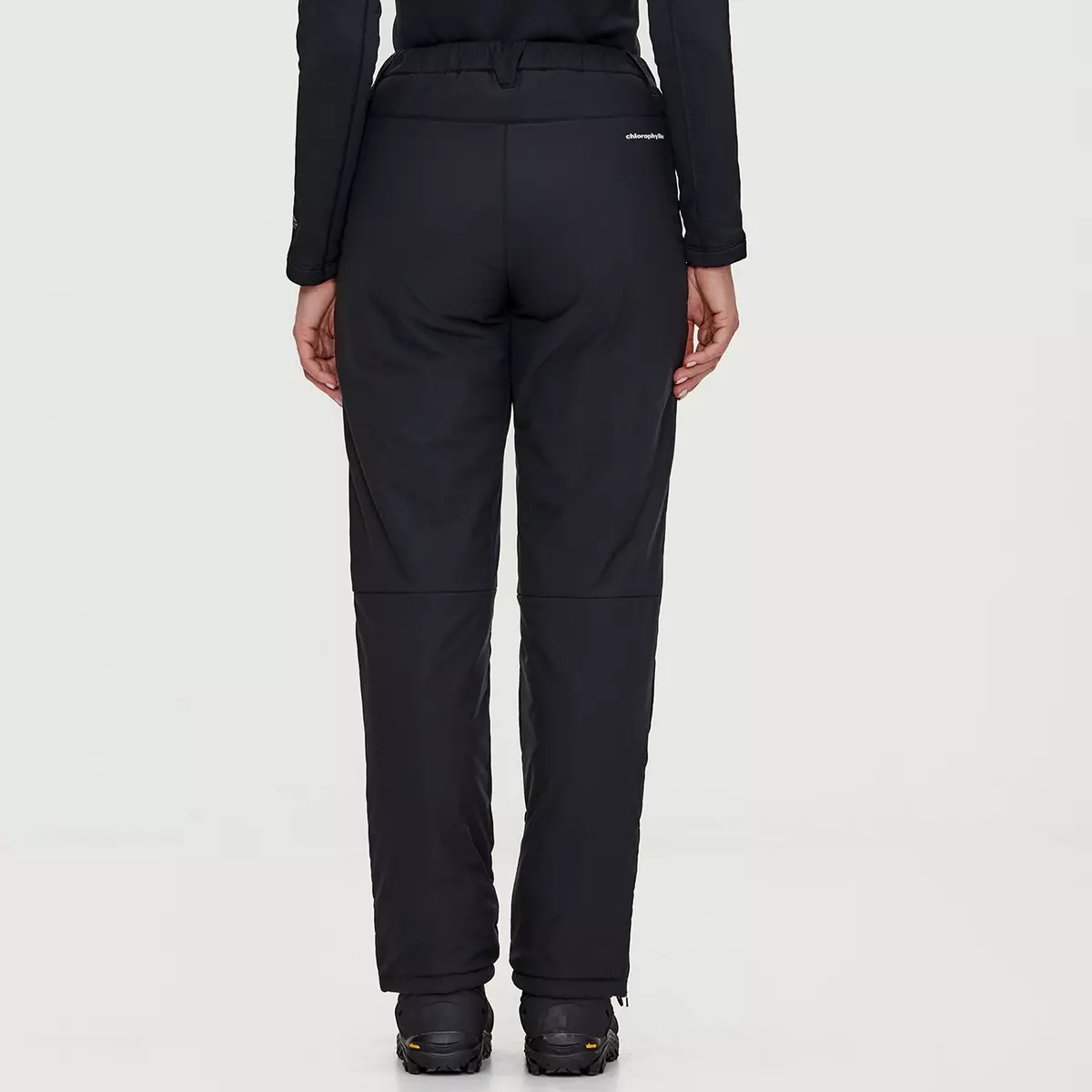 Vue arrière d'une personne portant un pantalon d'extérieur noir isolé et des chaussures noires, debout sur un fond gris clair. Le pantalon a un logo discret sur la ceinture et est doté de genoux articulés pour plus de flexibilité.