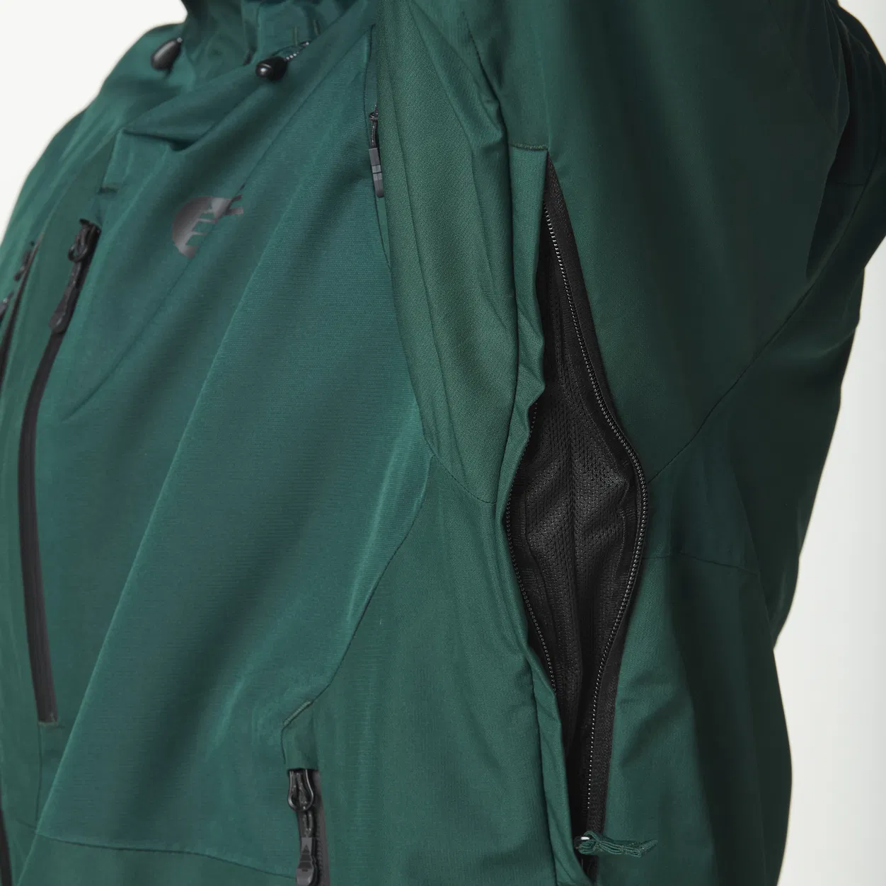 Gros plan d'une veste vert foncé mettant l'accent sur sa fonction de ventilation. L'image montre une zone ouverte sous le bras, révélant un tissu en maille noir conçu pour la respirabilité. La veste possède également une poche poitrine zippée.