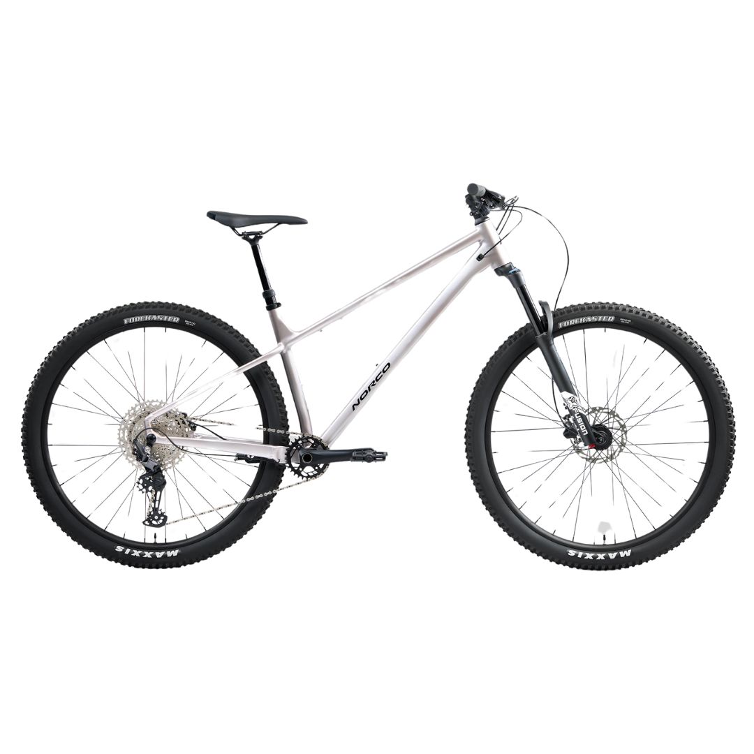 Un vélo de montagne argenté avec une selle noire, un guidon noir, de larges pneus à crampons, une fourche à suspension avant et des freins à disque, représenté de profil sur fond blanc.