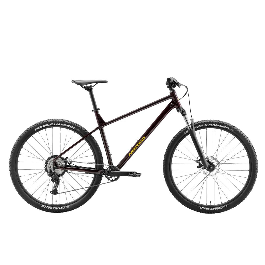 Un vélo de montagne Norco STORM noir avec logo jaune, fourche suspendue à l'avant, freins à disque, guidon plat et gros pneus à crampons est représenté de profil sur un fond blanc.