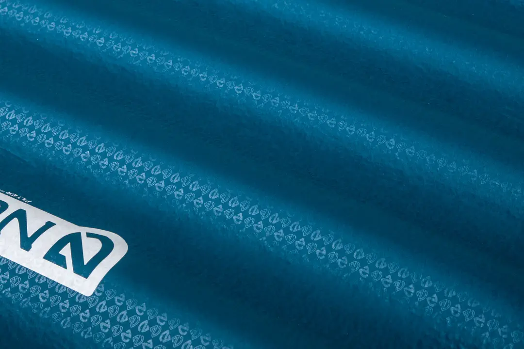 Vue rapprochée d'un matelas de couchage gonflable bleu avec des crêtes texturées et un logo blanc partiel dans le coin.