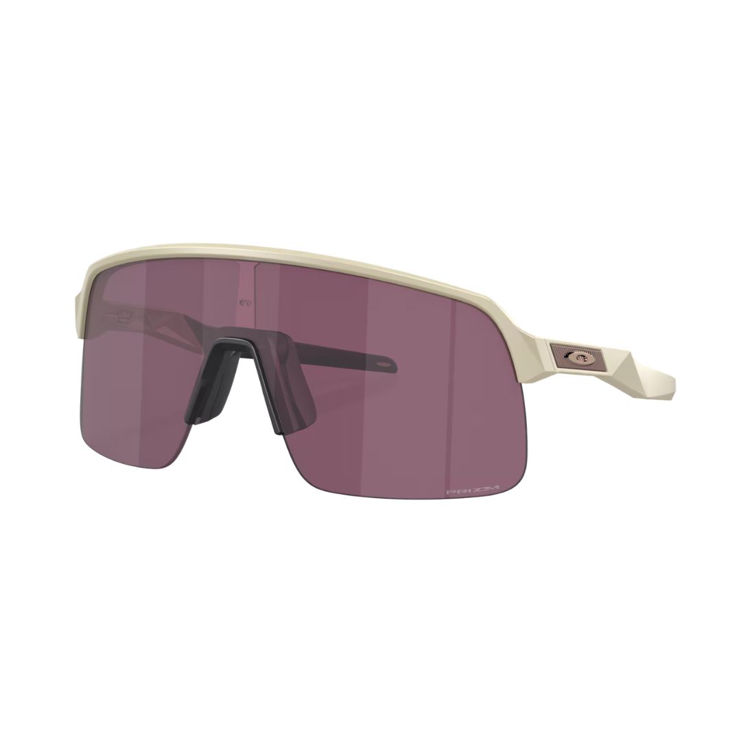 Les lunettes de soleil de sport SUTRO LITE MATTE SAND/PRIZM ROAD BLACK se caractérisent par une monture beige, un grand verre unique teinté de violet et des plaquettes nasales noires, le tout présenté sur fond blanc.