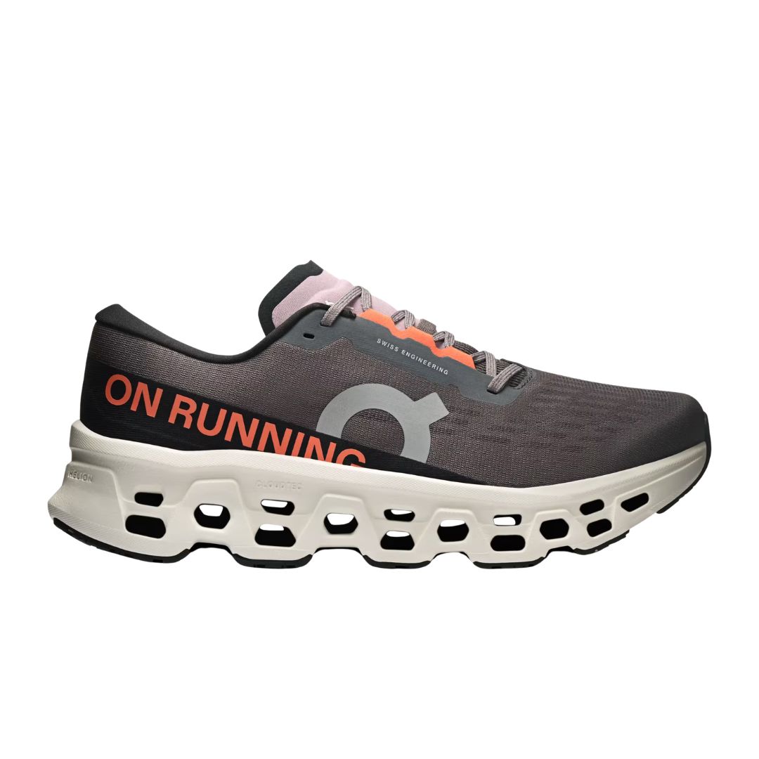 La CLOUDMONSTER 3 M est une chaussure de sport grise avec "ON RUNNING" en orange sur le côté, une semelle blanche géométrique avec de grandes découpes, ainsi que des accents noirs et roses.