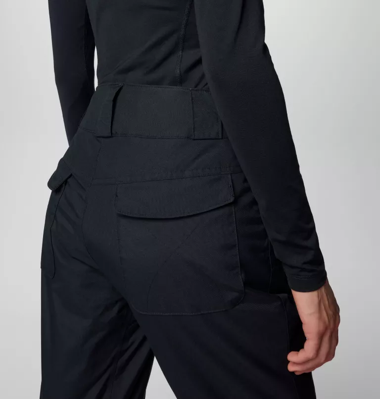 Une personne porte un haut noir à manches longues et un pantalon noir à taille haute, le dos tourné. Le pantalon a de grandes poches et l'accent est mis sur le bas du corps, montrant les détails du tissu et du design.