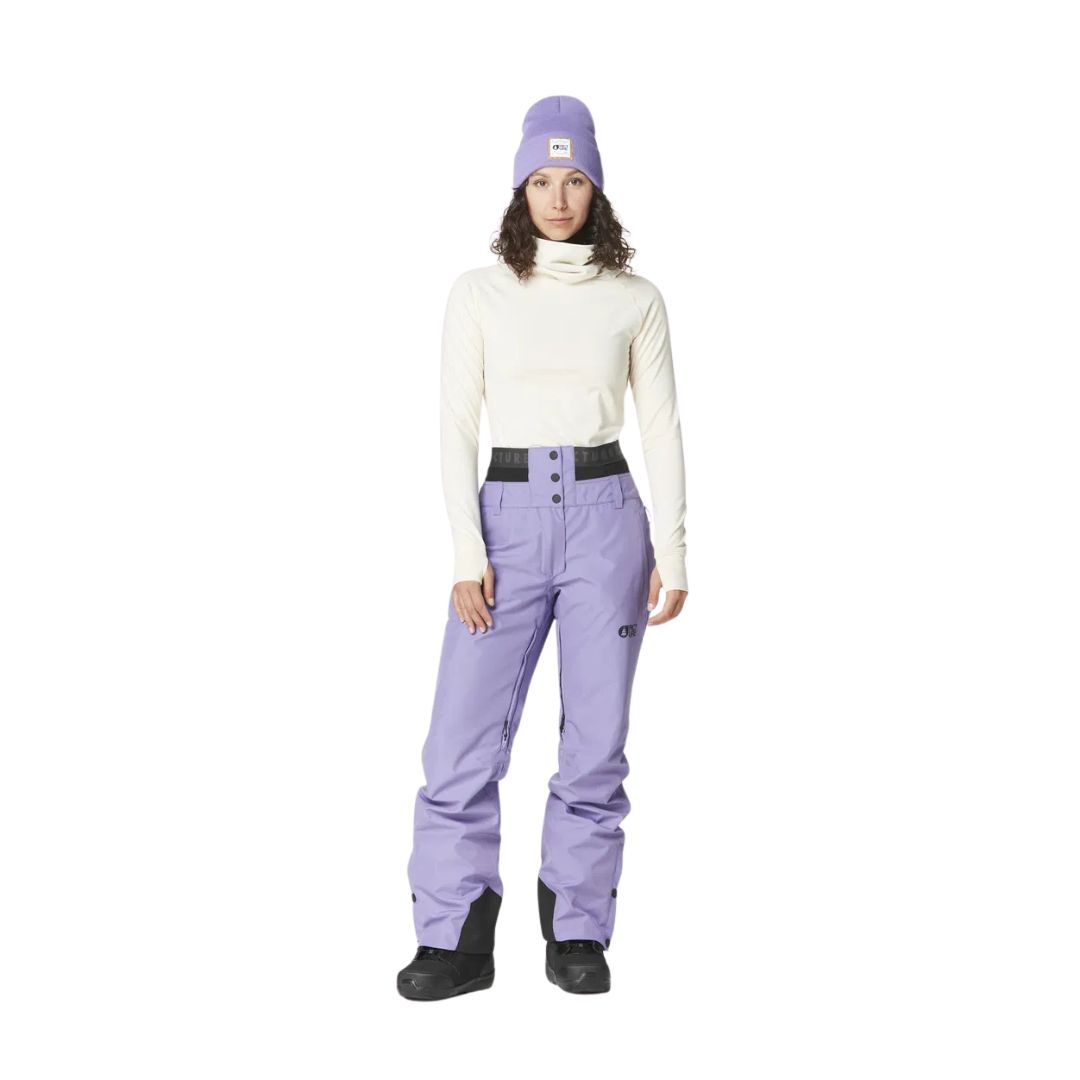 Une personne portant un col roulé blanc, un pantalon de neige violet, des bottes de neige noires et un bonnet violet se tient debout sur un fond blanc.