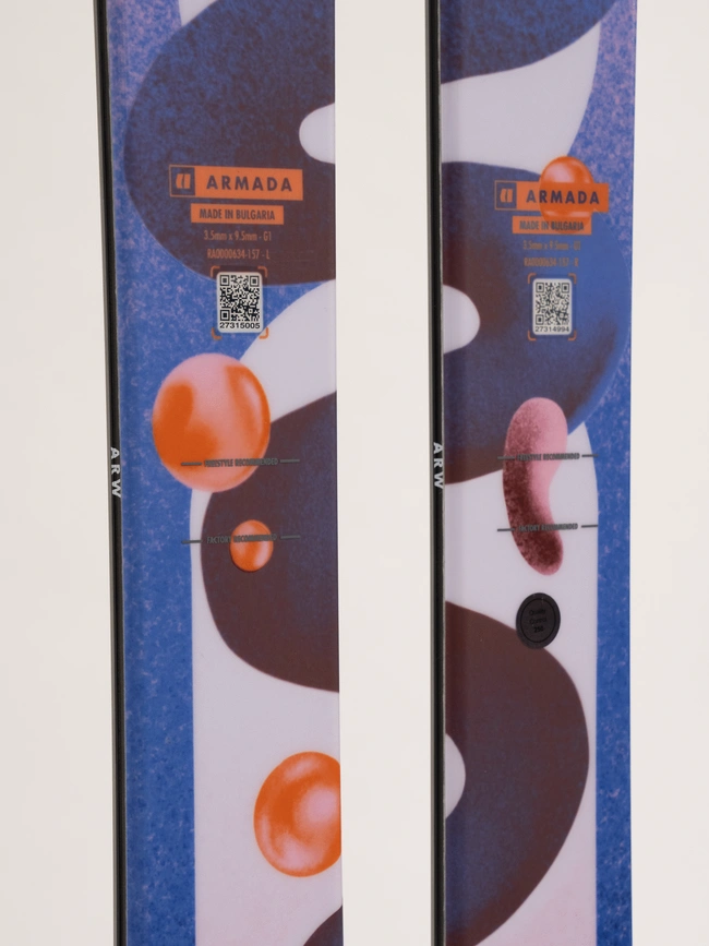 Gros plan de deux skis avec un motif abstrait coloré composé de formes orange, violettes et blanches. Les skis affichent le nom de la marque « Armada » ainsi que des codes QR et le texte « Fabriqué en Bulgarie ».