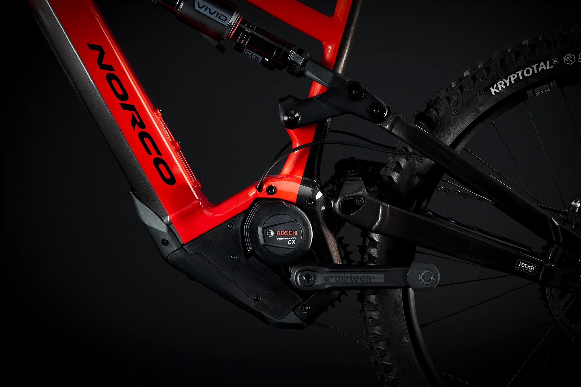 Gros plan d'un vélo de montagne électrique Norco rouge, montrant le moteur Bosch Performance CX, les détails du cadre, la suspension et la roue arrière avec un pneu Kryptoall sur un fond sombre.
