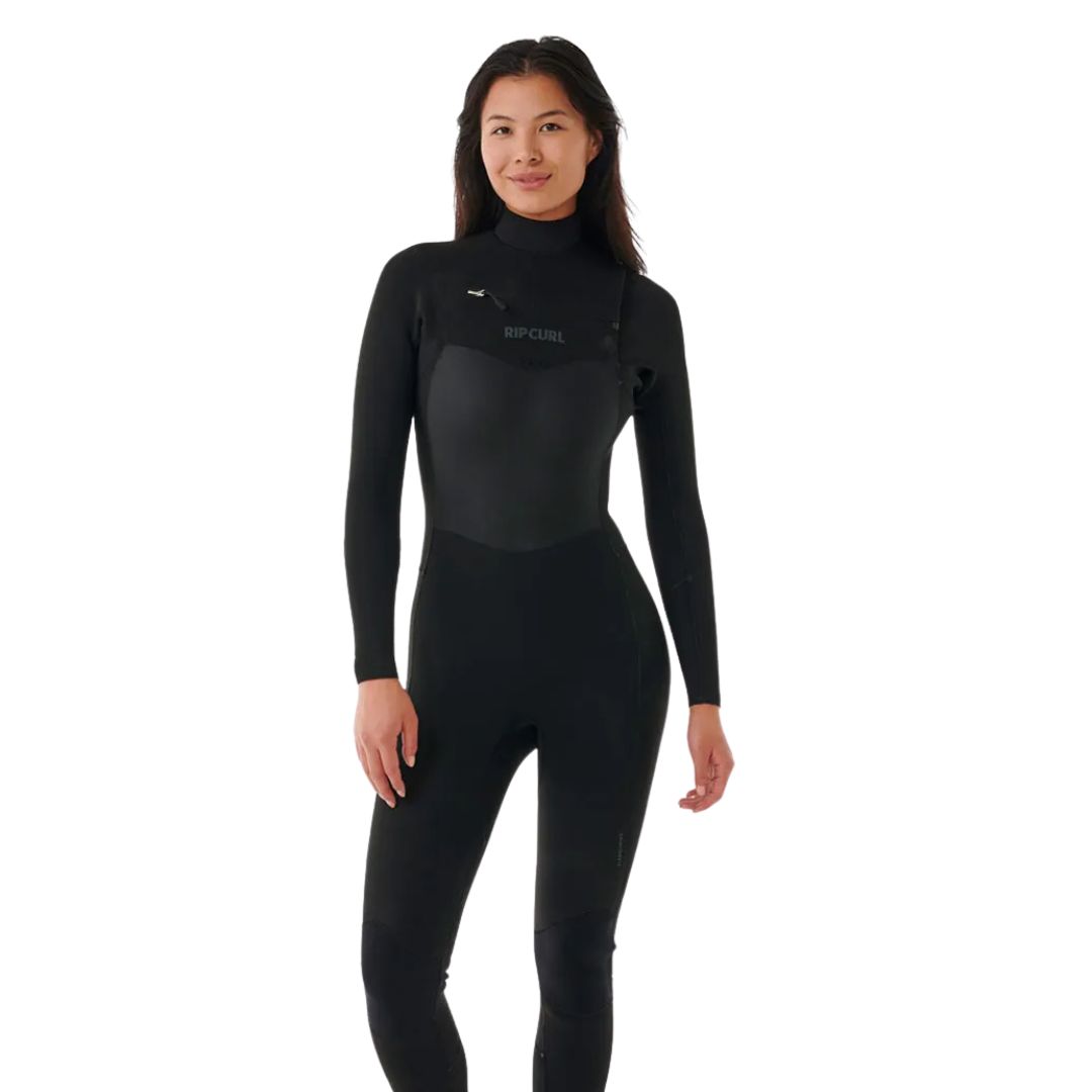 Une femme se tient debout et sourit alors qu'elle porte une combinaison de plongée noire à manches longues. La marque "Rip Curl" est imprimée sur la poitrine. L'arrière-plan est blanc.