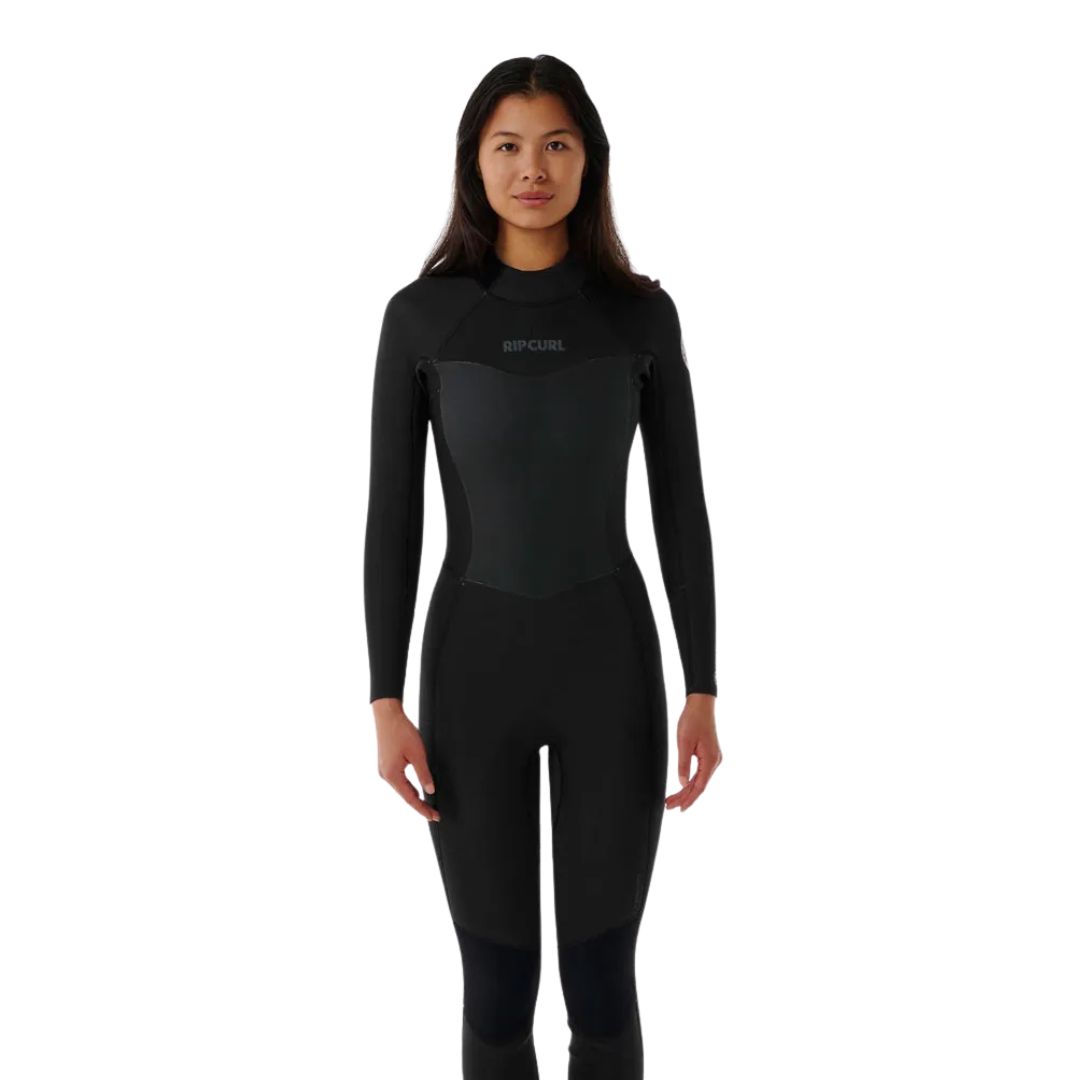 Une femme se tient debout, de face, vêtue d'une combinaison de plongée Rip Curl noire à manches longues et à jambes entières, sur un fond blanc uni.