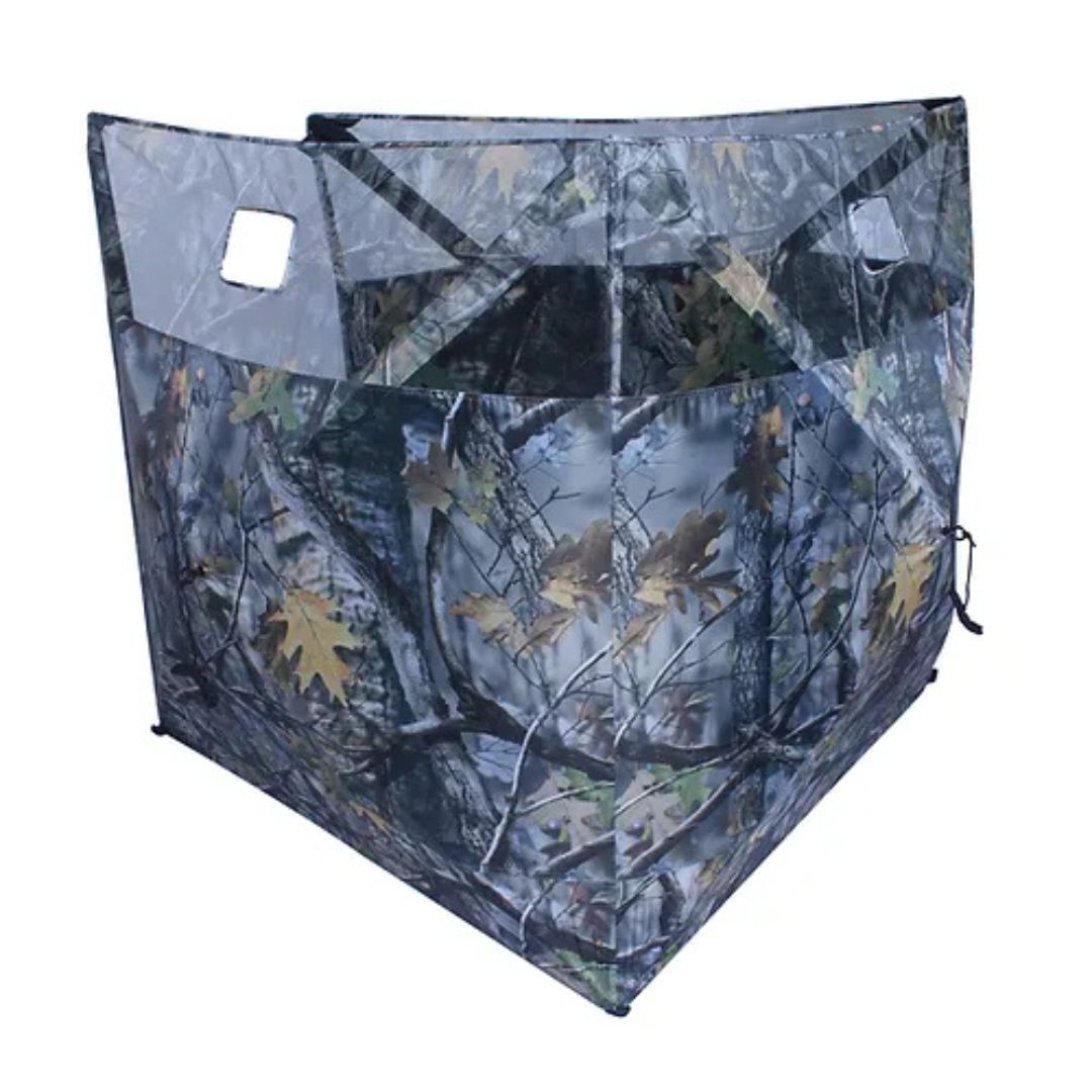 Un affût de chasse à panneaux avec un motif de camouflage représentant des feuilles et des branches, conçu avec des fenêtres à panneaux transparents et un cadre solide et incliné.