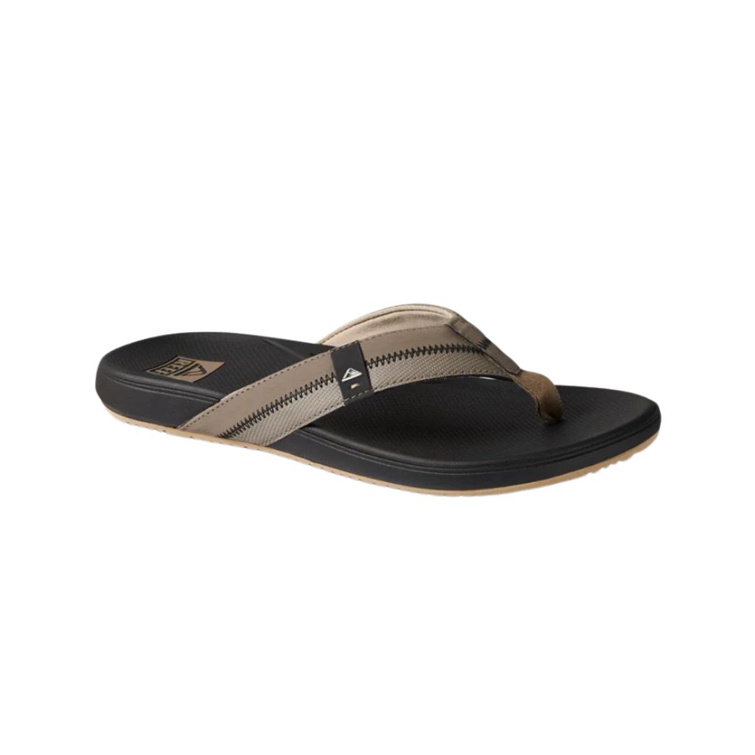 La GOUGOUNE REEF CUSHION PHANTOM 2.0 POUR HOMME est une tong simple avec une semelle noire, des brides en tissu beige avec des surpiqûres en zigzag et un petit logo sur le côté, offrant un style décontracté prêt pour la plage.
