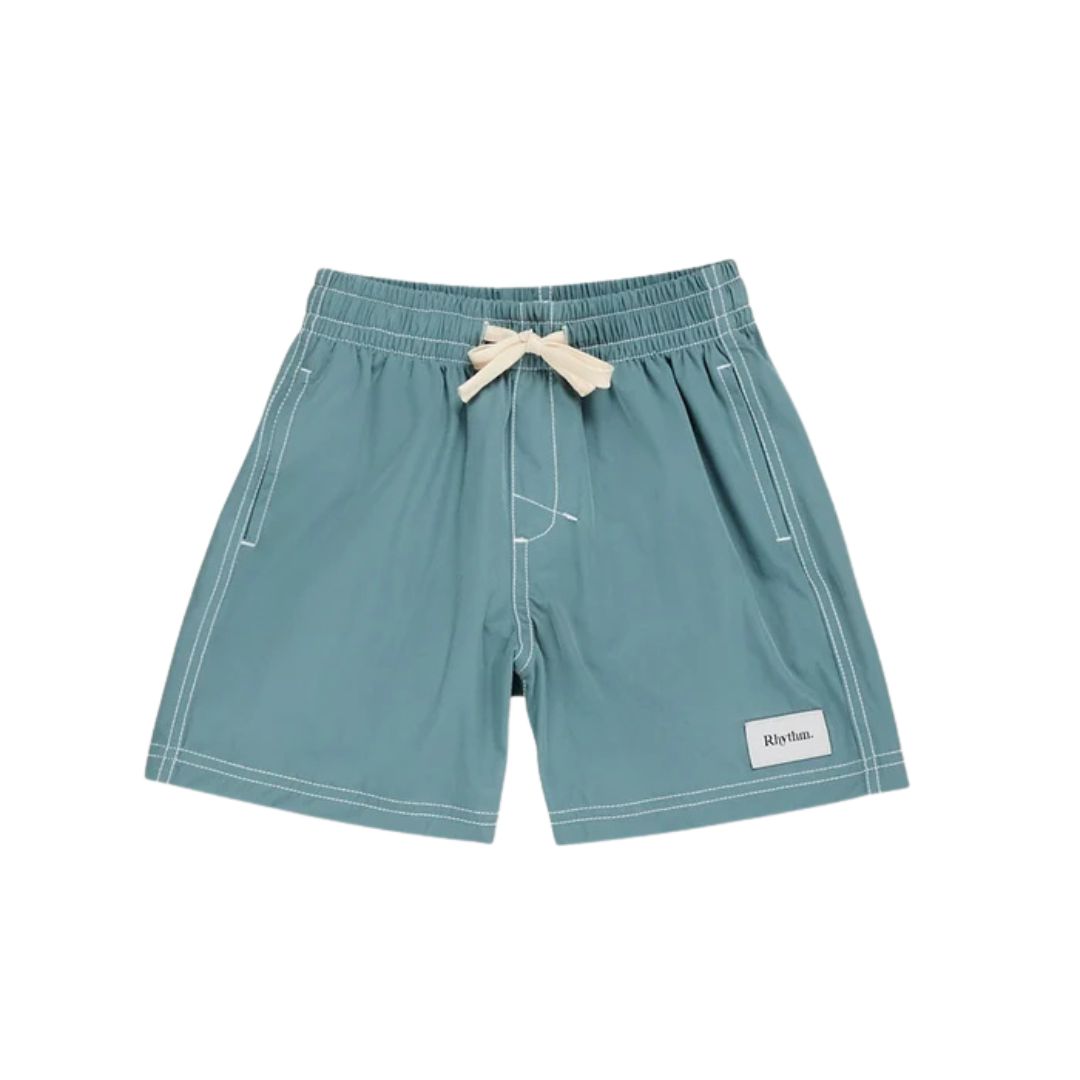 SHORT DE PLAGE CONTRASTÉ POUR ENFANTS, de couleur bleu sarcelle, avec des coutures blanches, un cordon de serrage crème à la taille et un petit écusson blanc « Rhythm » sur la jambe gauche. Le short est présenté à plat sur un fond blanc.