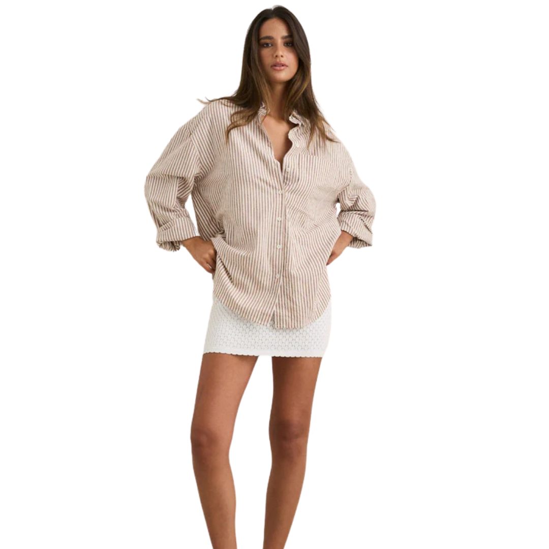 Une femme porte le VALLEY STRIPE OVERSIZED SHIRT avec une jupe blanche.