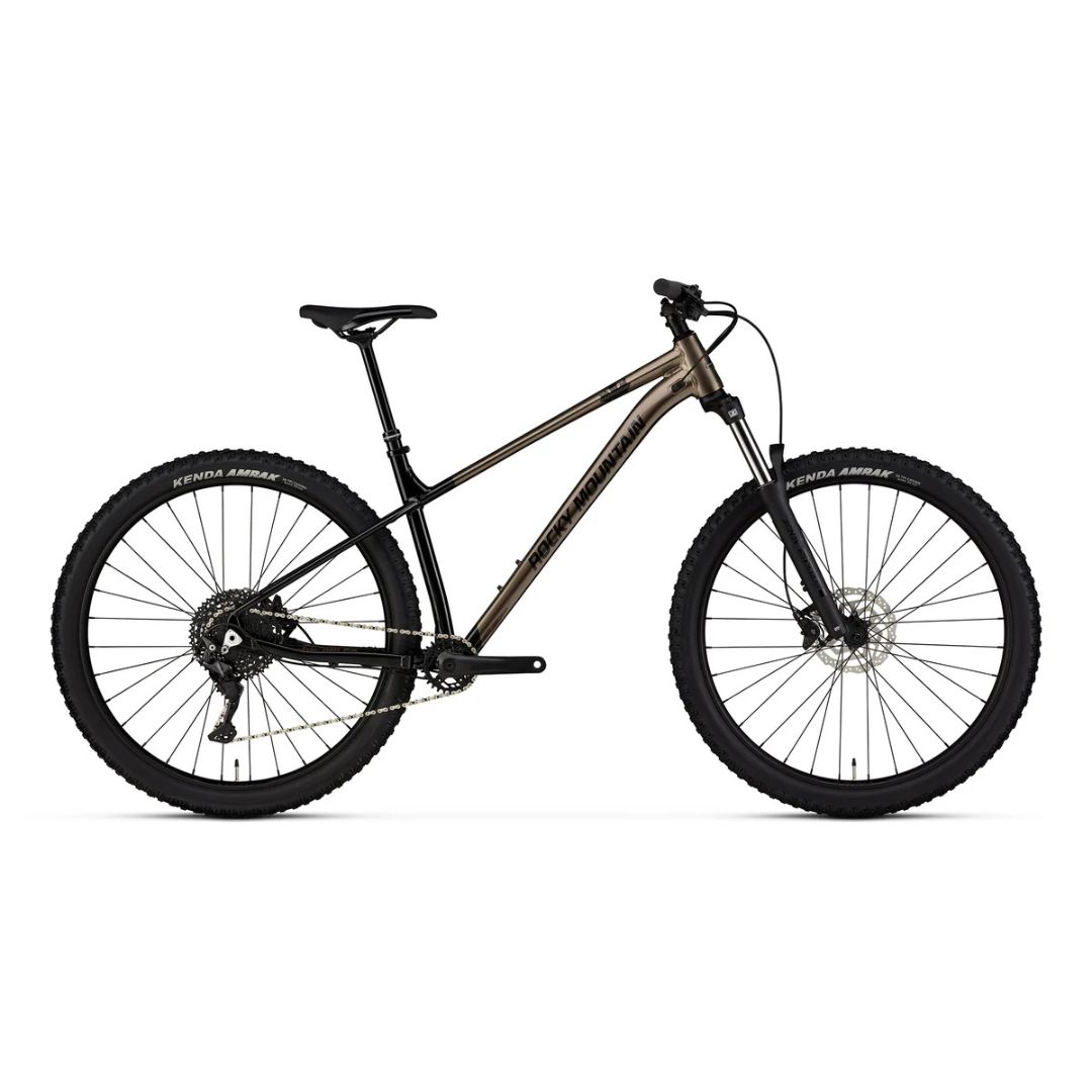 Un vélo de montagne marron métallisé avec un cadre rigide, une fourche à suspension avant, des freins à disque et des pneus à crampons, présenté dans une vue de profil latéral sur fond blanc.