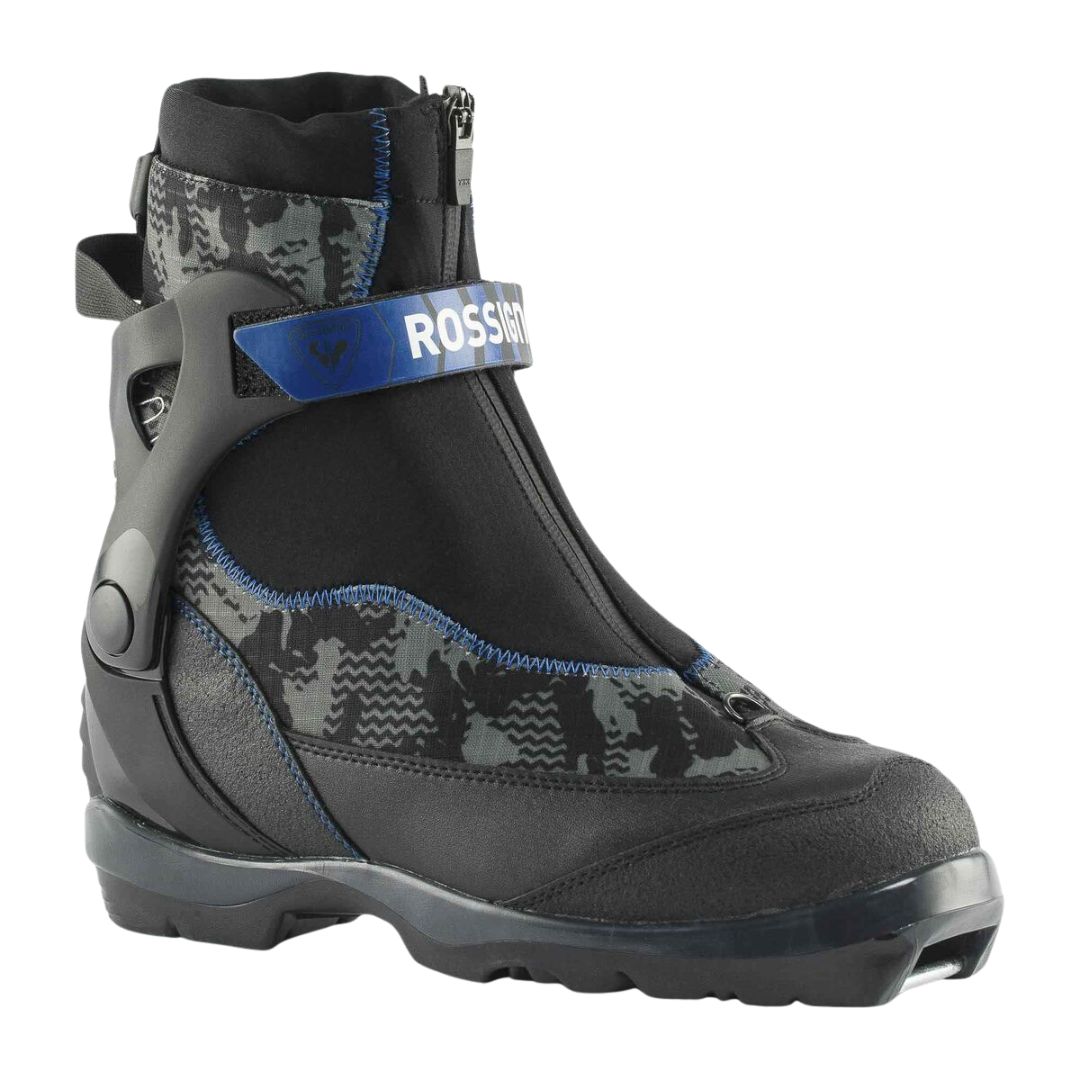La BC 6 FW est une chaussure de ski de fond noire et bleue avec une fermeture à glissière sur le devant, une bride de cheville portant la mention "ROSSIGNOL", une tige en tissu à motifs, un support de talon solide et une semelle robuste.
