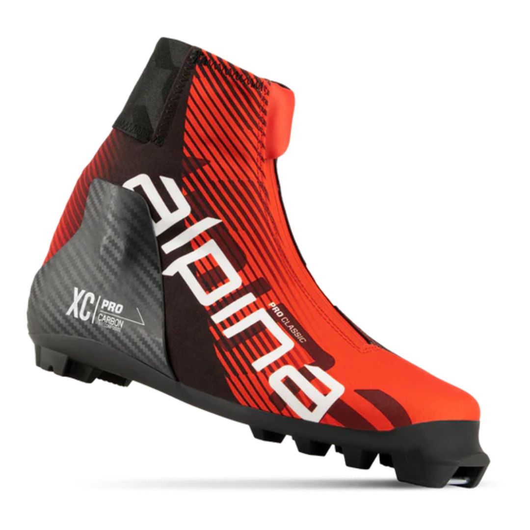 La BOTTE DE SKI DE FOND ALPINA PRO CLASSIC UNISEXE est une chaussure de ski de fond rouge et noire avec un marquage "alpina" audacieux, un support de talon en carbone, un cache-lacet zippé marqué "XC PRO CARBON" et une semelle robuste pour les fixations.